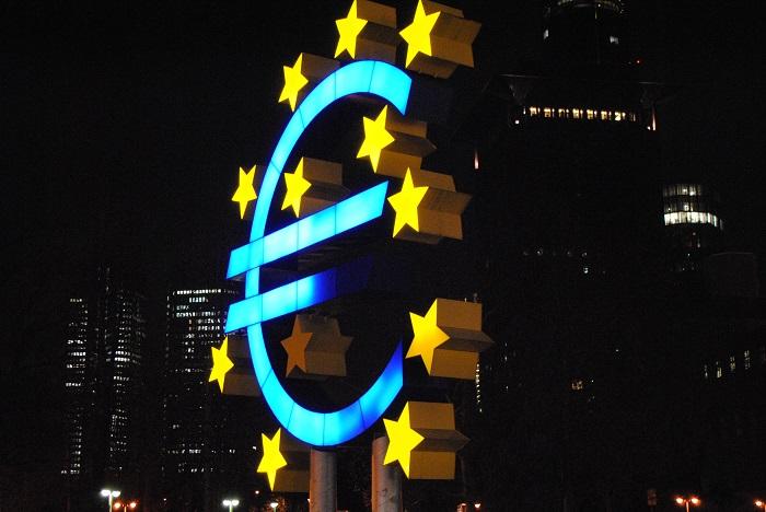 Euro sign on blue surrounded by yellow stars with a city skyline at night 