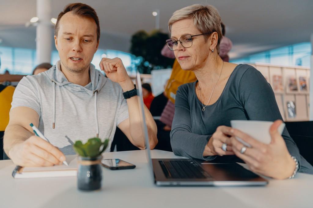 DVV:n digituen kuvituskuvia. Kaksi henkilöä juovat keskustelevat tietokoneen ääressä, toisella on kahvikuppi kädessä.