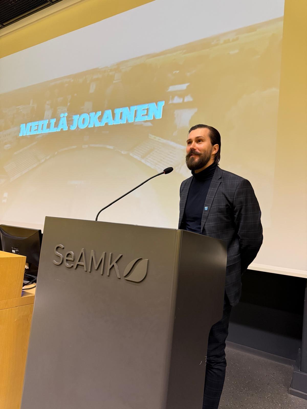 Henkilö pitää esitystä yleisölle puhujanpöntöstä.