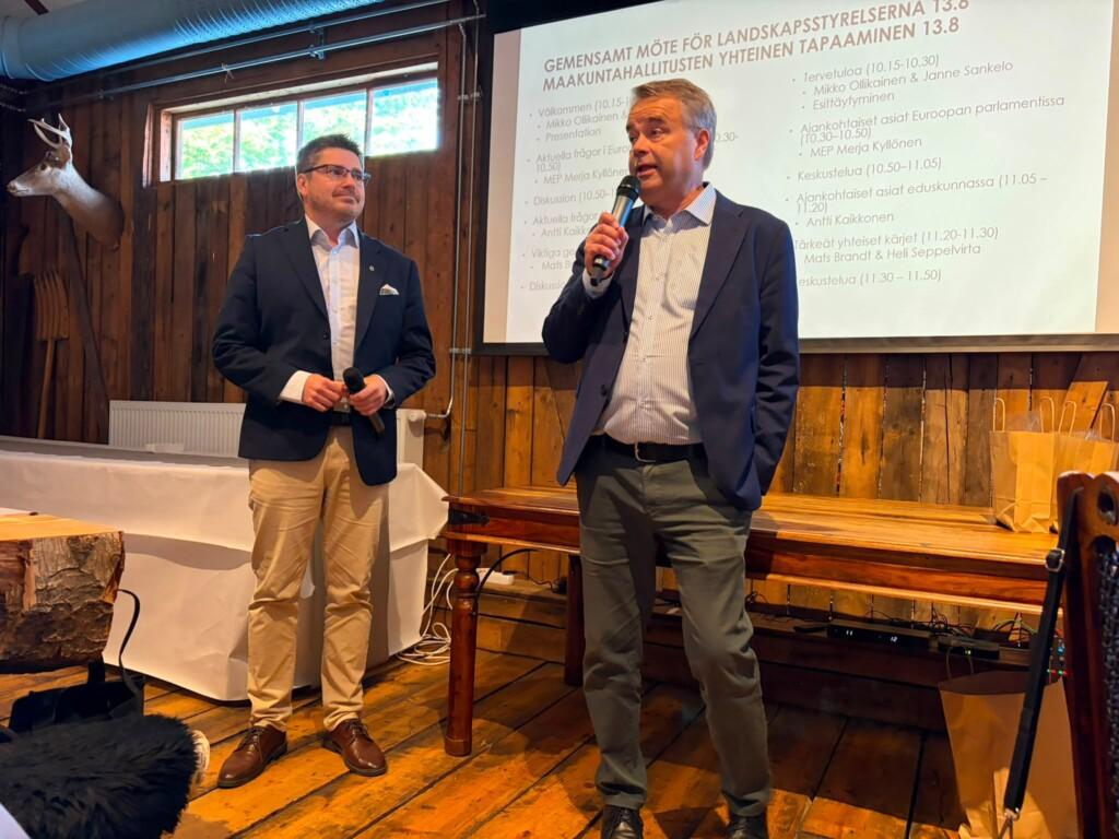 Kaksi henkilöä puheenvuorossa kokoustilan etuosassa.